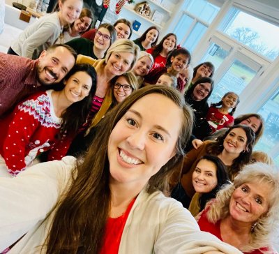 Woman smiling taking a selfie with her coworkers behind her 