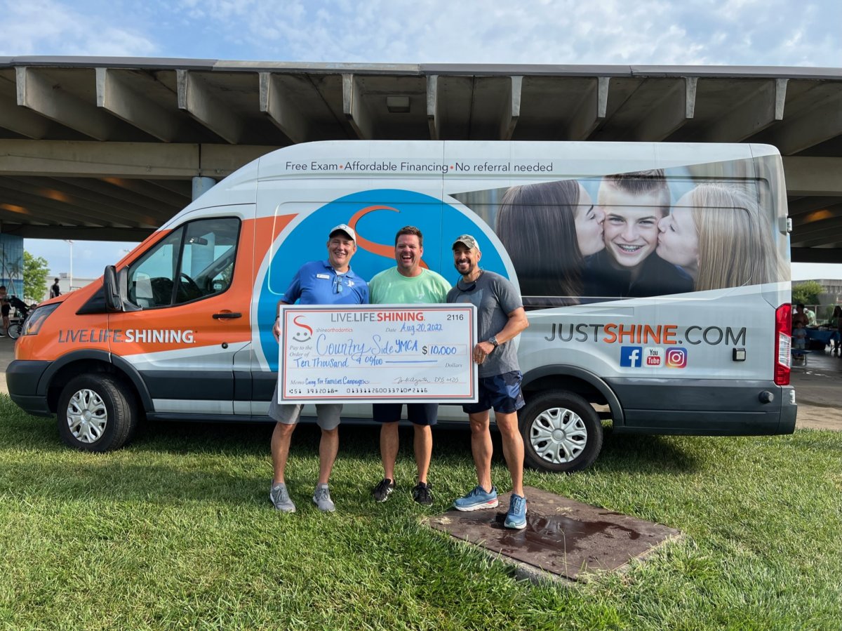 Men standing next to van holding a big check 
